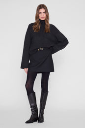 Black mini skirt with belt detail, styled with black turtleneck and knee-high boots.
