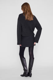 Black mini skirt worn with charcoal sweater and black boots, rear view.