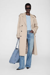 Pale blue cropped tee with framed monogram worn under a beige trench coat and blue jeans.