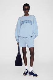 Pale blue short-framed sweatshirt and shorts set with monogram text print, styled with navy bag and sneakers.