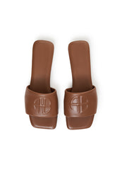Pair of cognac brown leather slides with embossed logo on upper strap, shown from above.