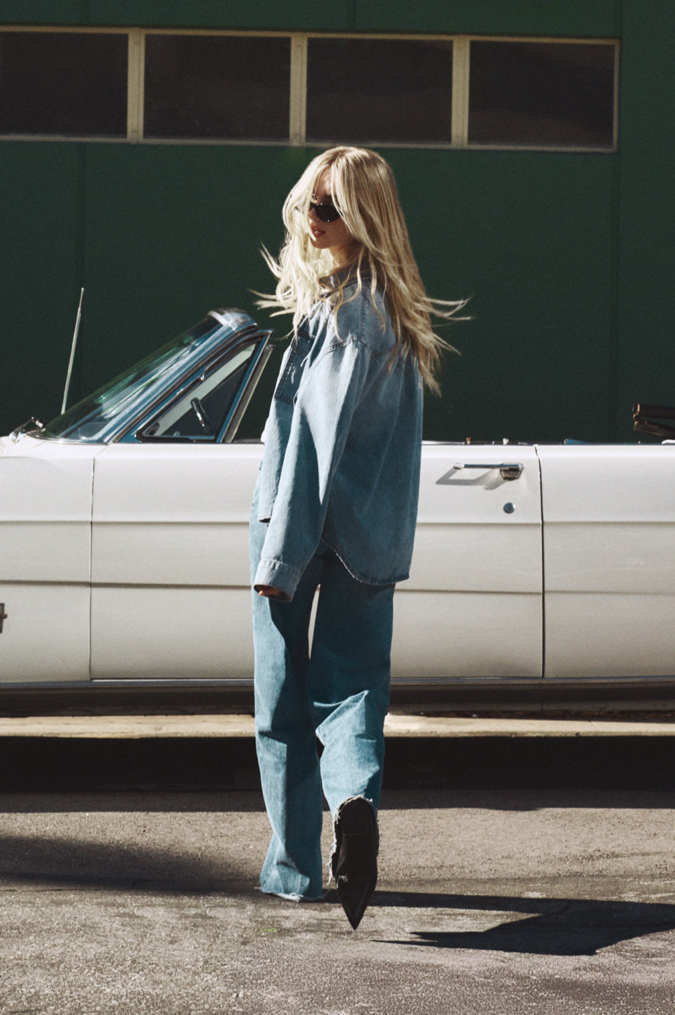 Woman in a blue suit walking past a vintage car.