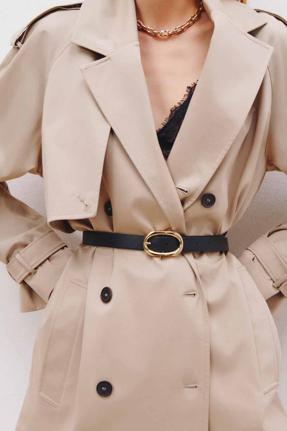 Beige trench coat with black belt and gold buckle on a white background