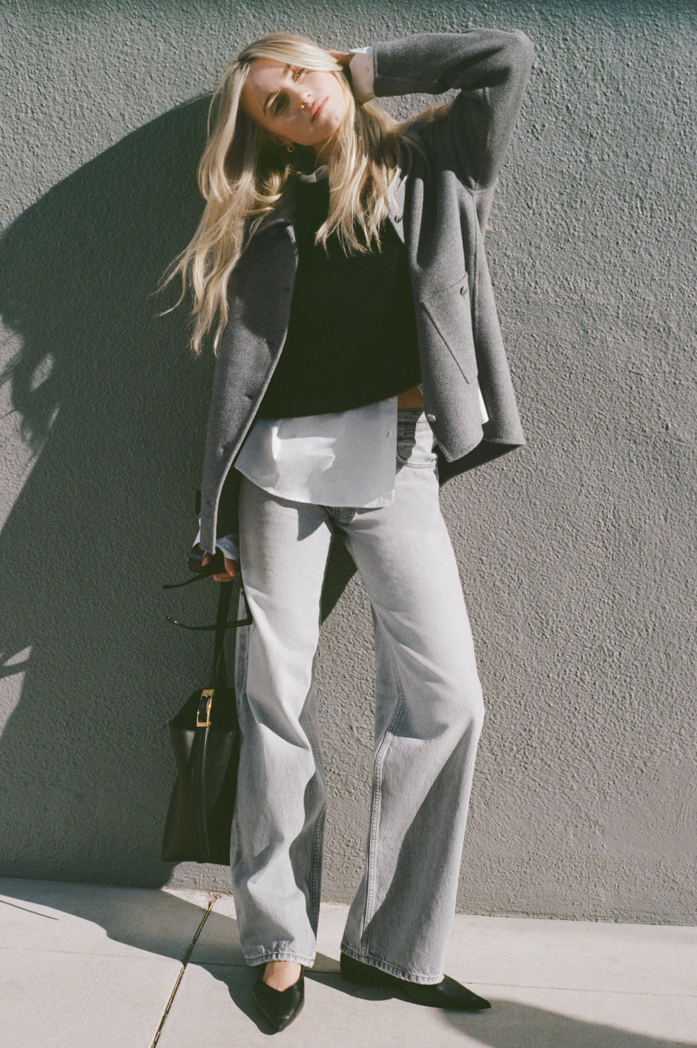 Woman in gray coat and pants standing against a gray wall
